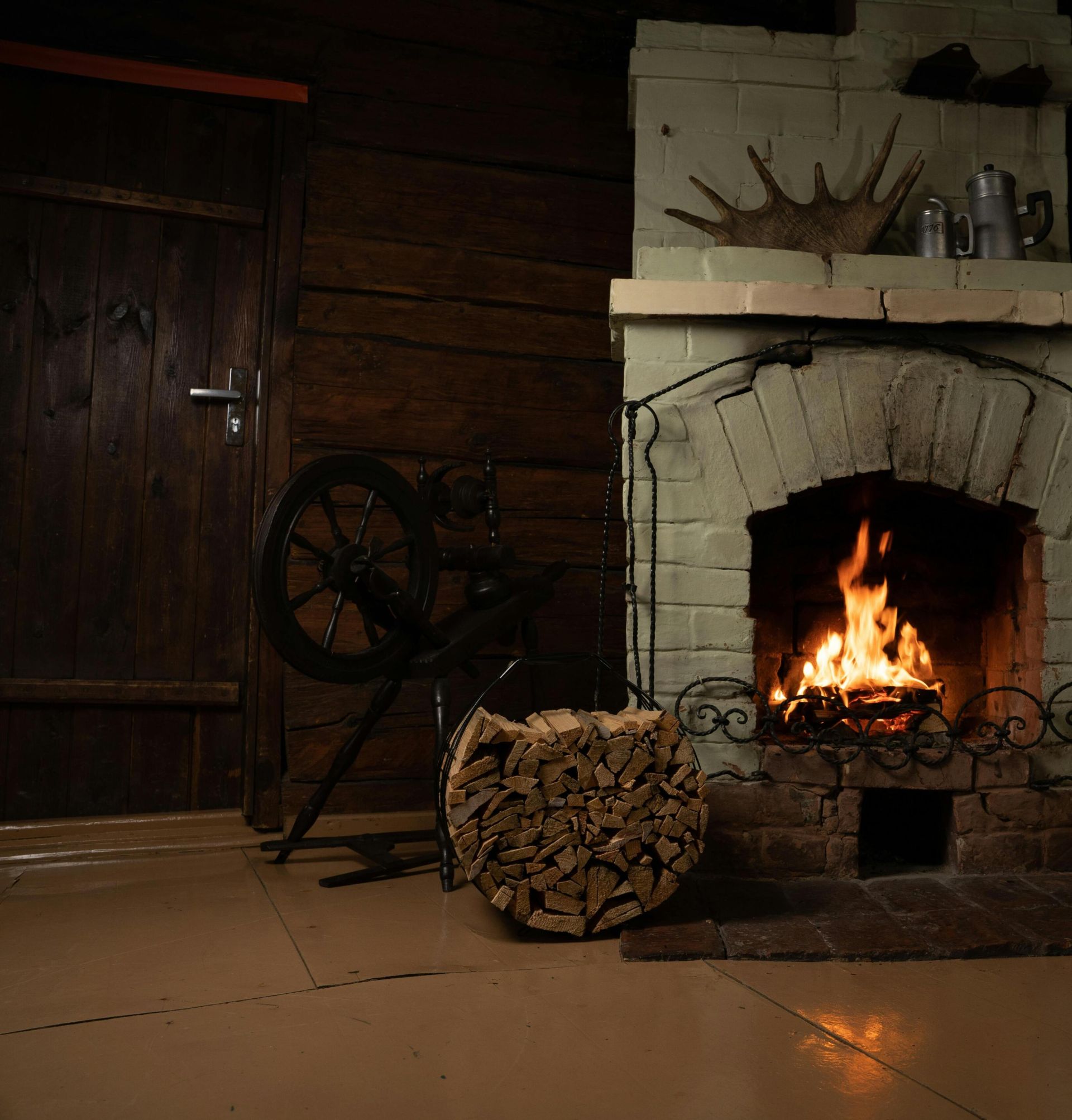 Warm rustic room featuring a brick fireplace with roaring fire, logs, and vintage decor.