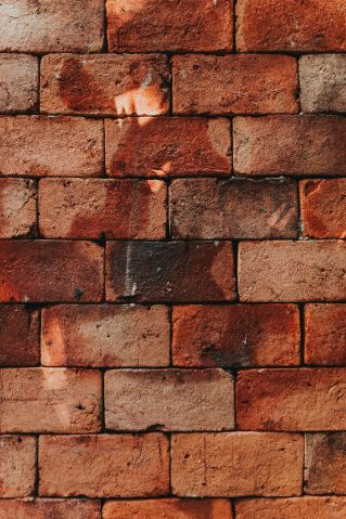 A detailed view of a weathered red brick wall showcasing rustic textures and shadows.
